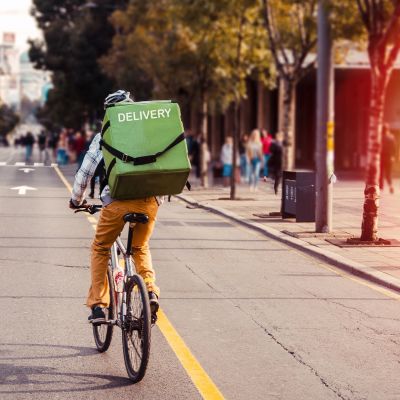 Delivery man food service courier on bicycle in town. Rear view of man riding a bicycle in the city street with green bag on back